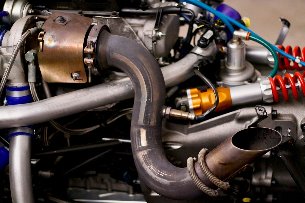 A wideband oxygen sensor fitted into the exhaust pipe of a motorsport engine, with the sensor cable running back across the engine bay